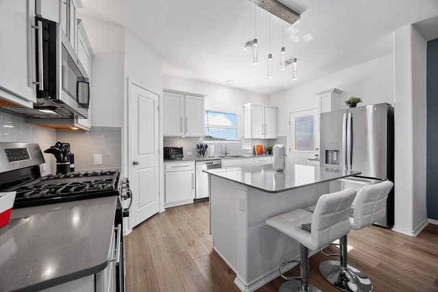 kitchen featuring a kitchen island, pendant lighting, white cabinets, light hardwood / wood-style floors, and stainless steel appliances