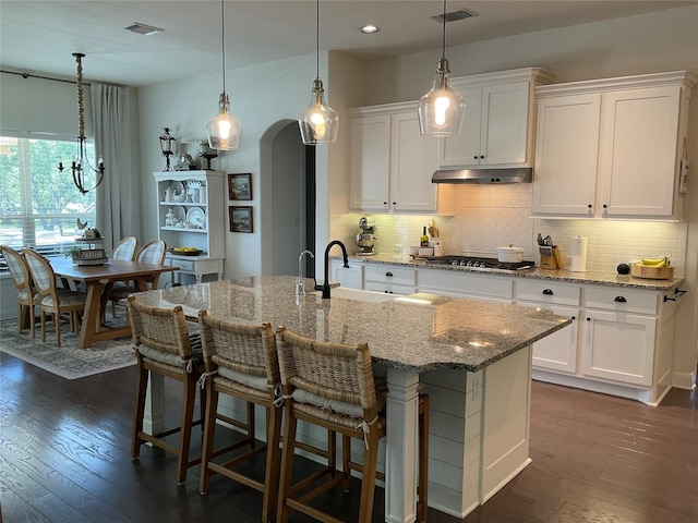 kitchen with a kitchen island with sink, sink, light stone countertops, and white cabinets