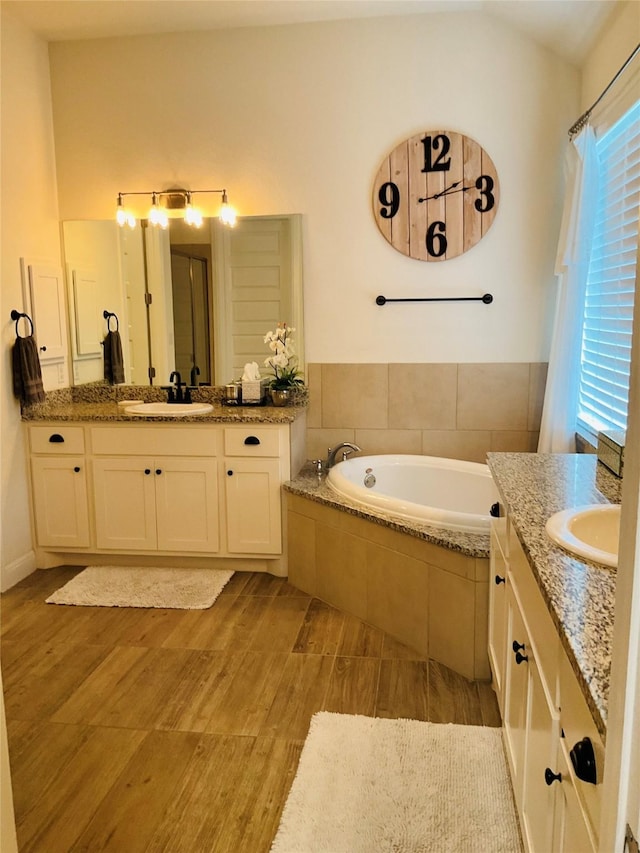 bathroom with a relaxing tiled tub, vanity, and plenty of natural light