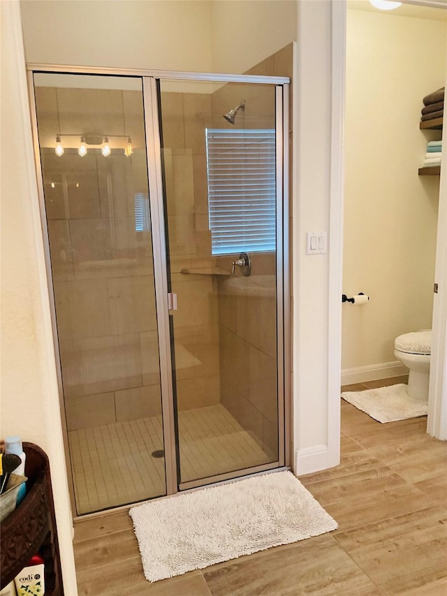 bathroom with wood-type flooring, toilet, and a shower with door