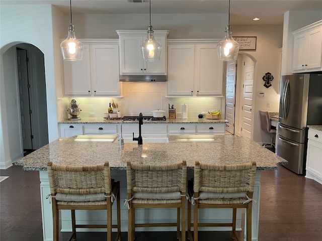 kitchen with a kitchen bar, white cabinetry, decorative light fixtures, appliances with stainless steel finishes, and a kitchen island with sink