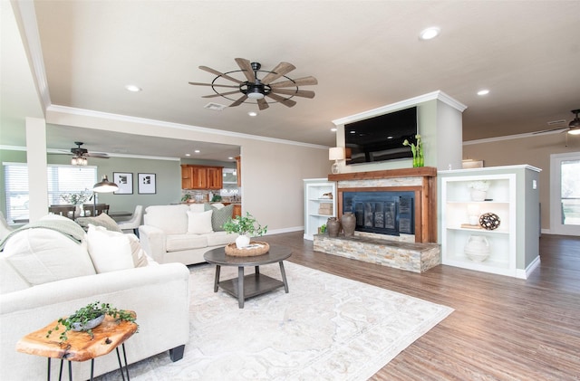 living room featuring a fireplace, ornamental molding, ceiling fan, and light wood-type flooring