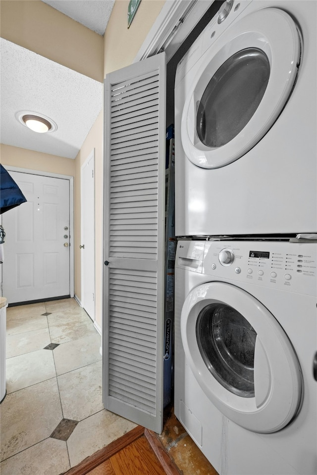 laundry room featuring stacked washer and dryer, light tile patterned floors, and a textured ceiling