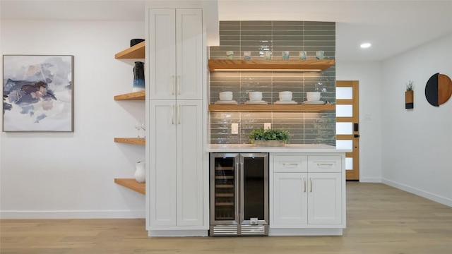 bar featuring wine cooler, white cabinetry, decorative backsplash, and light wood-type flooring