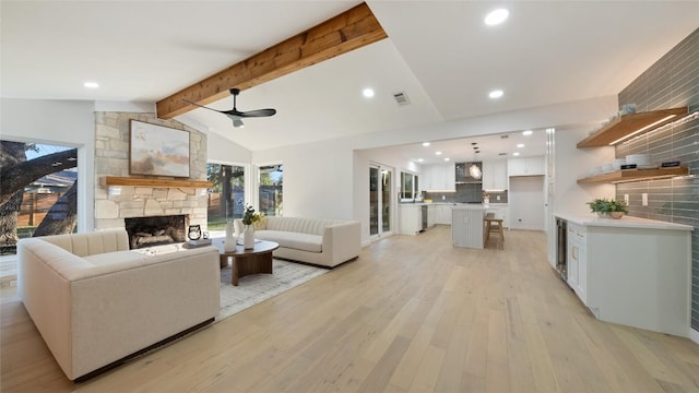 living room featuring ceiling fan, a fireplace, light hardwood / wood-style floors, and vaulted ceiling with beams