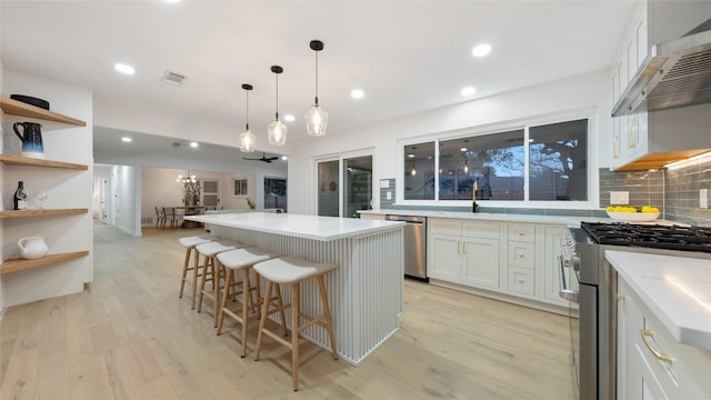 kitchen with appliances with stainless steel finishes, white cabinetry, a kitchen island, a kitchen bar, and wall chimney exhaust hood