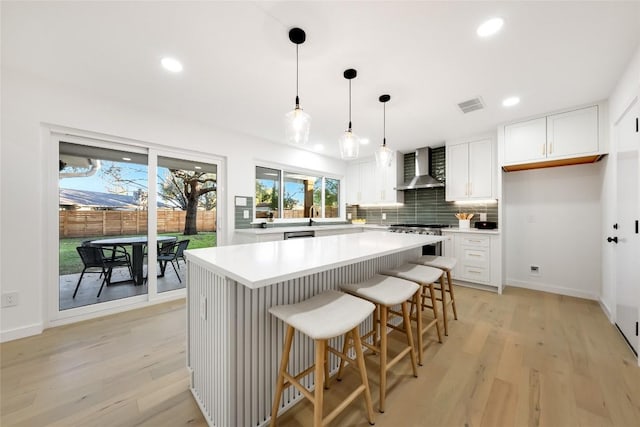 kitchen featuring wall chimney range hood, decorative light fixtures, white cabinets, and a kitchen island