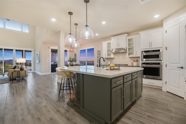 125 Serene Hilltop Cir, Austin, TX 78738 - kitchen with under cabinet range hood, white cabinets, light countertops, wood finished floors, and a kitchen island with sink