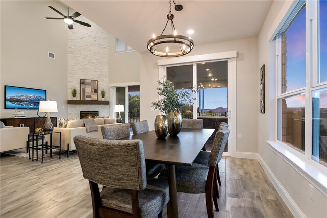 125 Serene Hilltop Cir, Austin, TX 78738 - dining area featuring a chandelier, light wood-style floors, a fireplace, a high ceiling, and ceiling fan