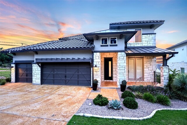 125 Serene Hilltop Cir, Austin, TX 78738 - view of front facade with stone siding, an attached garage, a standing seam roof, driveway, and stucco siding