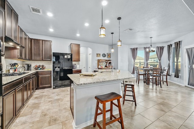 kitchen featuring dark brown cabinetry, a breakfast bar, sink, black refrigerator with ice dispenser, and a center island with sink