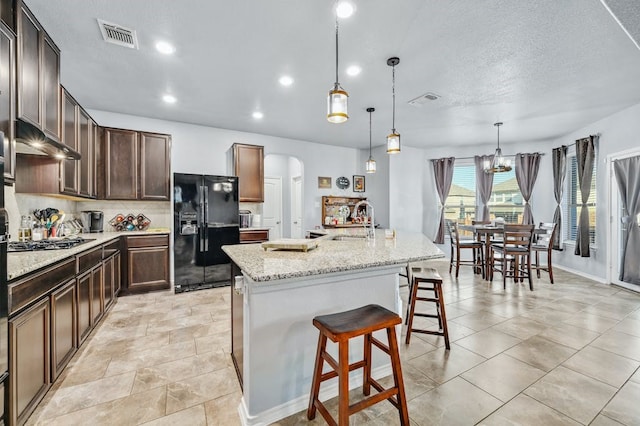 1712 Uhland Dr, Leander, TX 78641 - kitchen featuring black refrigerator with ice dispenser, arched walkways, tasteful backsplash, a kitchen breakfast bar, and a kitchen island with sink