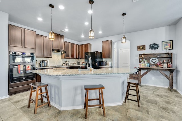 kitchen featuring a kitchen island with sink, light stone counters, pendant lighting, and black appliances