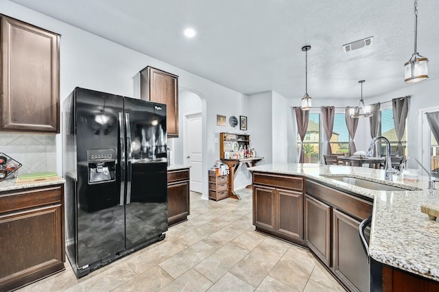 kitchen with pendant lighting, sink, light stone counters, black fridge with ice dispenser, and dark brown cabinets