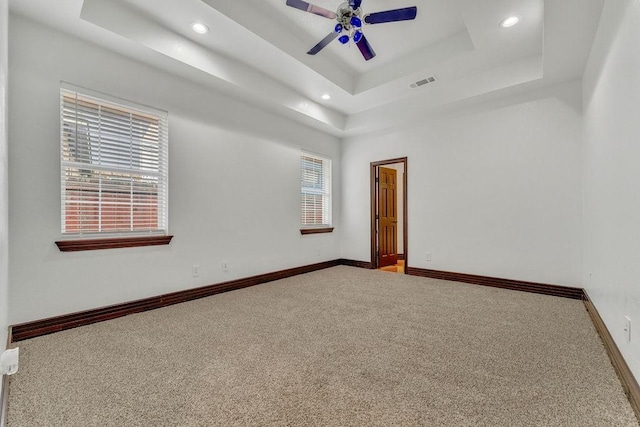 empty room featuring a tray ceiling, ceiling fan, and carpet flooring