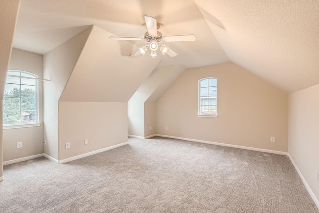 additional living space featuring light carpet, a textured ceiling, vaulted ceiling, and ceiling fan