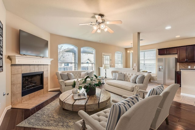 living room with dark hardwood / wood-style flooring, a textured ceiling, a tile fireplace, and ceiling fan