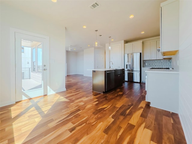 kitchen featuring pendant lighting, a kitchen island with sink, stainless steel appliances, tasteful backsplash, and white cabinets