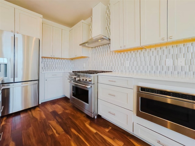 kitchen with white cabinets, backsplash, stainless steel appliances, dark wood-type flooring, and wall chimney exhaust hood