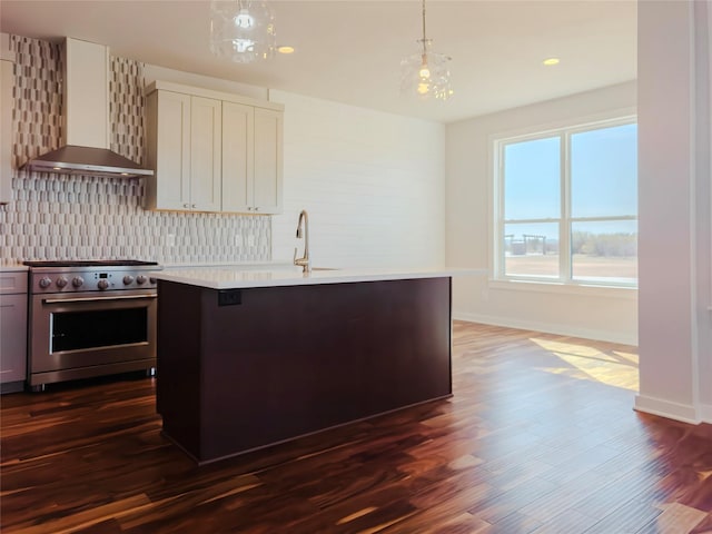 kitchen featuring pendant lighting, wall chimney range hood, stainless steel range, and a center island with sink