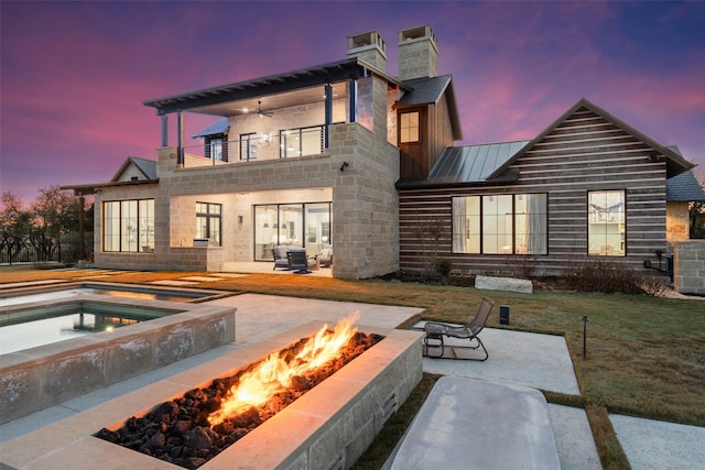 back house at dusk featuring a lawn, ceiling fan, a patio area, a pool, and a balcony