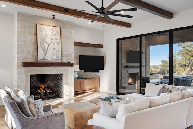 living room with ceiling fan, a stone fireplace, wood-type flooring, and beamed ceiling