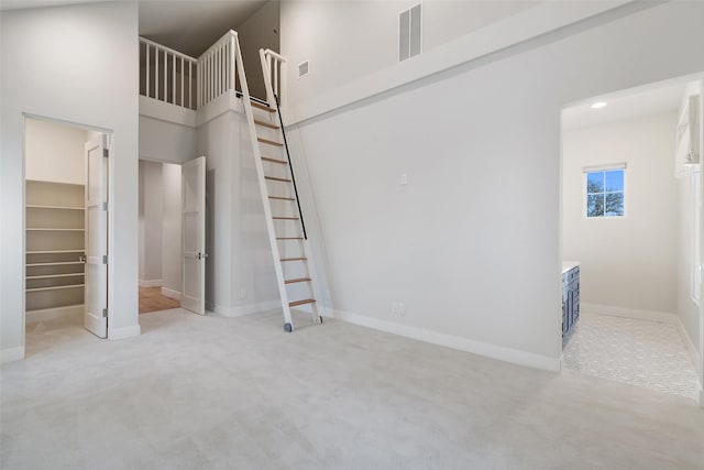 unfurnished bedroom with a spacious closet, light carpet, and a high ceiling