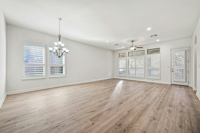 unfurnished living room featuring ceiling fan with notable chandelier, a healthy amount of sunlight, and light hardwood / wood-style floors