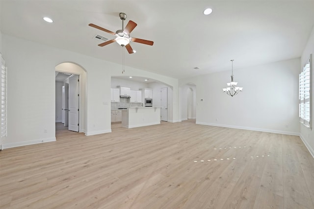 unfurnished living room featuring ceiling fan with notable chandelier and light hardwood / wood-style flooring