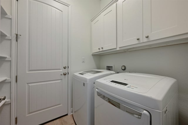 clothes washing area featuring separate washer and dryer, light hardwood / wood-style flooring, and cabinets