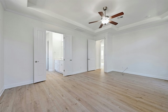 unfurnished bedroom with a tray ceiling, ensuite bathroom, ceiling fan, and light wood-type flooring