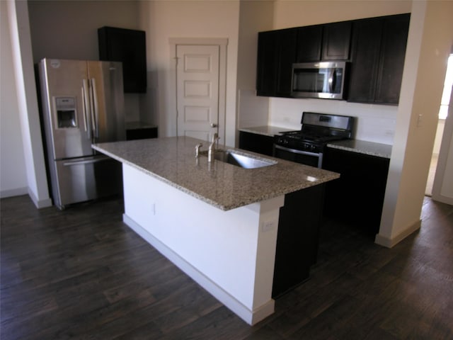 kitchen featuring dark hardwood / wood-style floors, sink, stainless steel appliances, light stone countertops, and a center island with sink