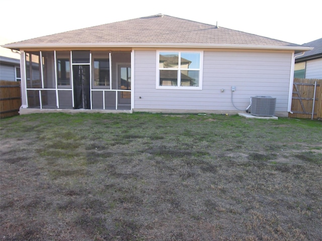 rear view of house with central AC, a sunroom, and a lawn