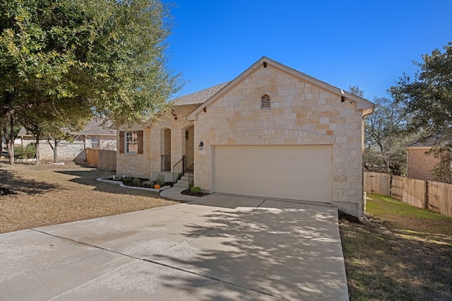 view of front of home featuring concrete driveway, stone siding, an attached garage, and fence