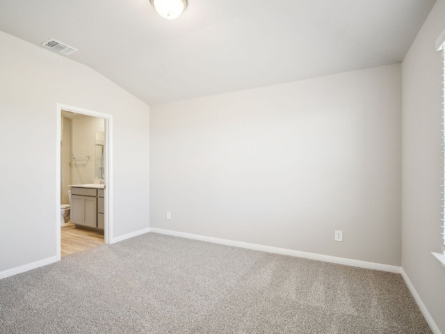 unfurnished bedroom with baseboards, visible vents, connected bathroom, light colored carpet, and lofted ceiling