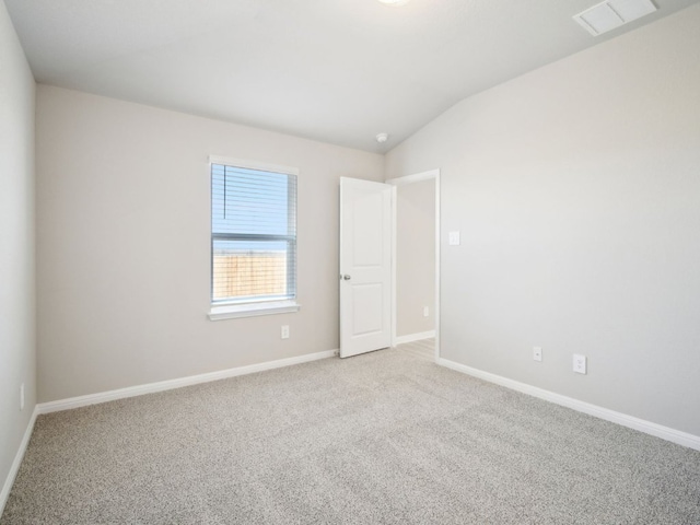 empty room featuring light colored carpet, visible vents, vaulted ceiling, and baseboards