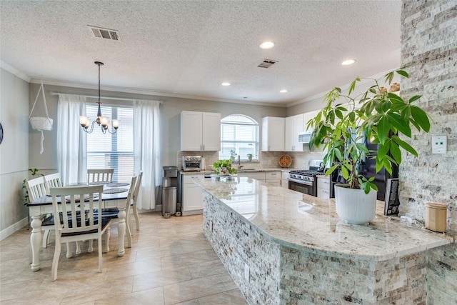 kitchen featuring stainless steel gas range, white cabinetry, hanging light fixtures, light stone countertops, and a textured ceiling