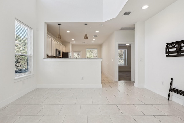 interior space with white cabinetry, hanging light fixtures, light tile patterned floors, light stone counters, and kitchen peninsula