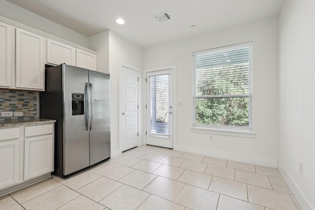 kitchen with light tile patterned floors, stainless steel fridge, backsplash, light stone counters, and white cabinets