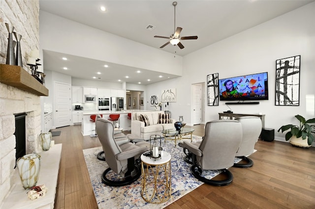 living room featuring a fireplace, visible vents, a high ceiling, dark wood-type flooring, and ceiling fan