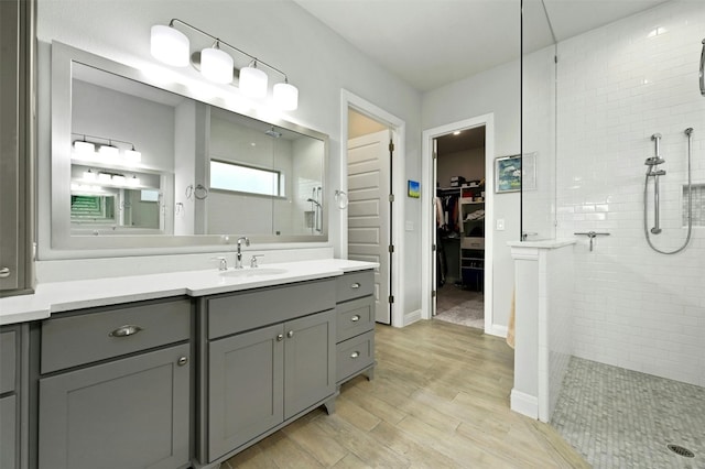 bathroom with baseboards, wood finished floors, a walk in closet, walk in shower, and vanity