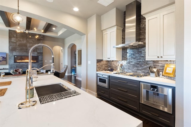 kitchen featuring pendant lighting, wall chimney range hood, gas cooktop, a tile fireplace, and white cabinetry