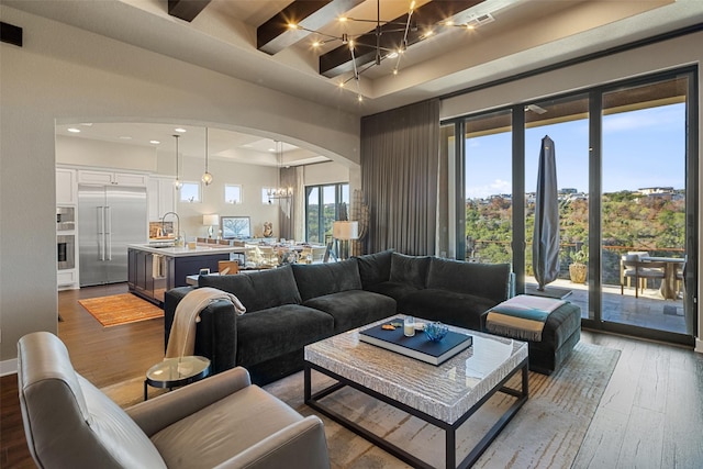 living room featuring sink, wood-type flooring, a chandelier, and a healthy amount of sunlight