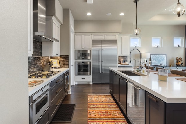 kitchen featuring wall chimney exhaust hood, sink, white cabinetry, an island with sink, and stainless steel appliances