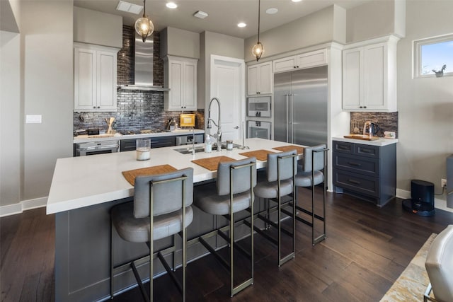 kitchen with stainless steel built in refrigerator, pendant lighting, white cabinets, and wall chimney exhaust hood