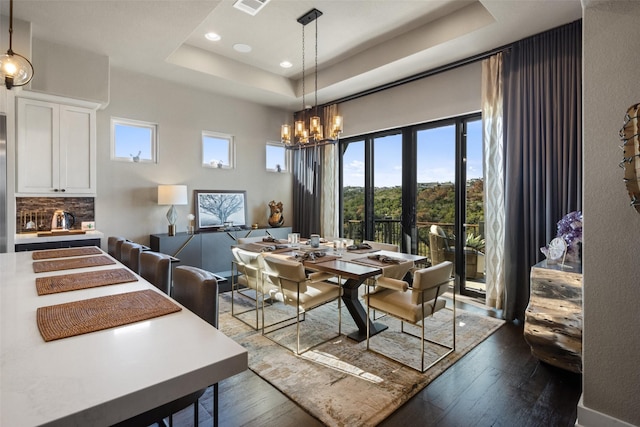 dining area featuring plenty of natural light, a tray ceiling, dark hardwood / wood-style flooring, and a notable chandelier