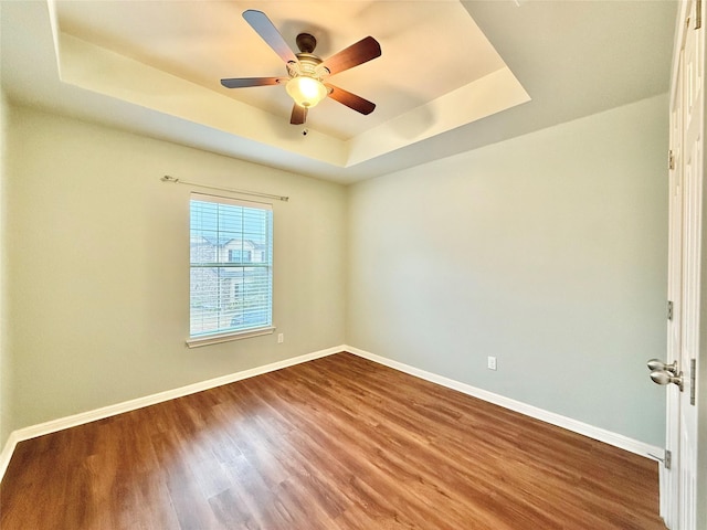 empty room featuring ceiling fan, wood-type flooring, and a raised ceiling