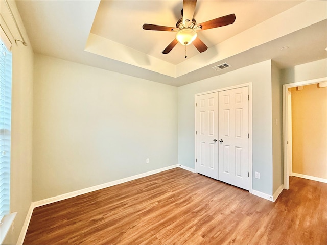 unfurnished bedroom featuring a tray ceiling, light hardwood / wood-style floors, a closet, and ceiling fan