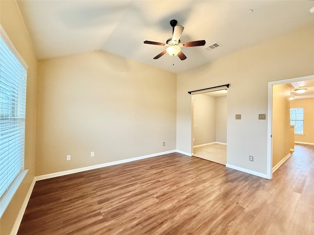 unfurnished bedroom featuring vaulted ceiling, a barn door, ceiling fan, and light wood-type flooring