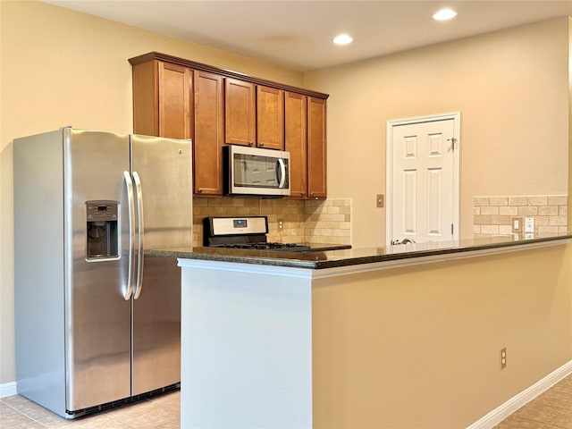 kitchen featuring appliances with stainless steel finishes, dark stone countertops, decorative backsplash, light tile patterned floors, and kitchen peninsula